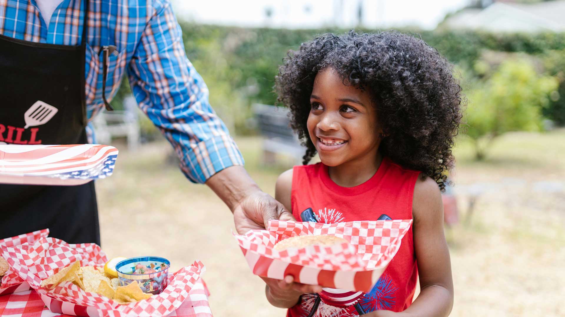 Young boy in red shirt carrying hamburger in BBQ