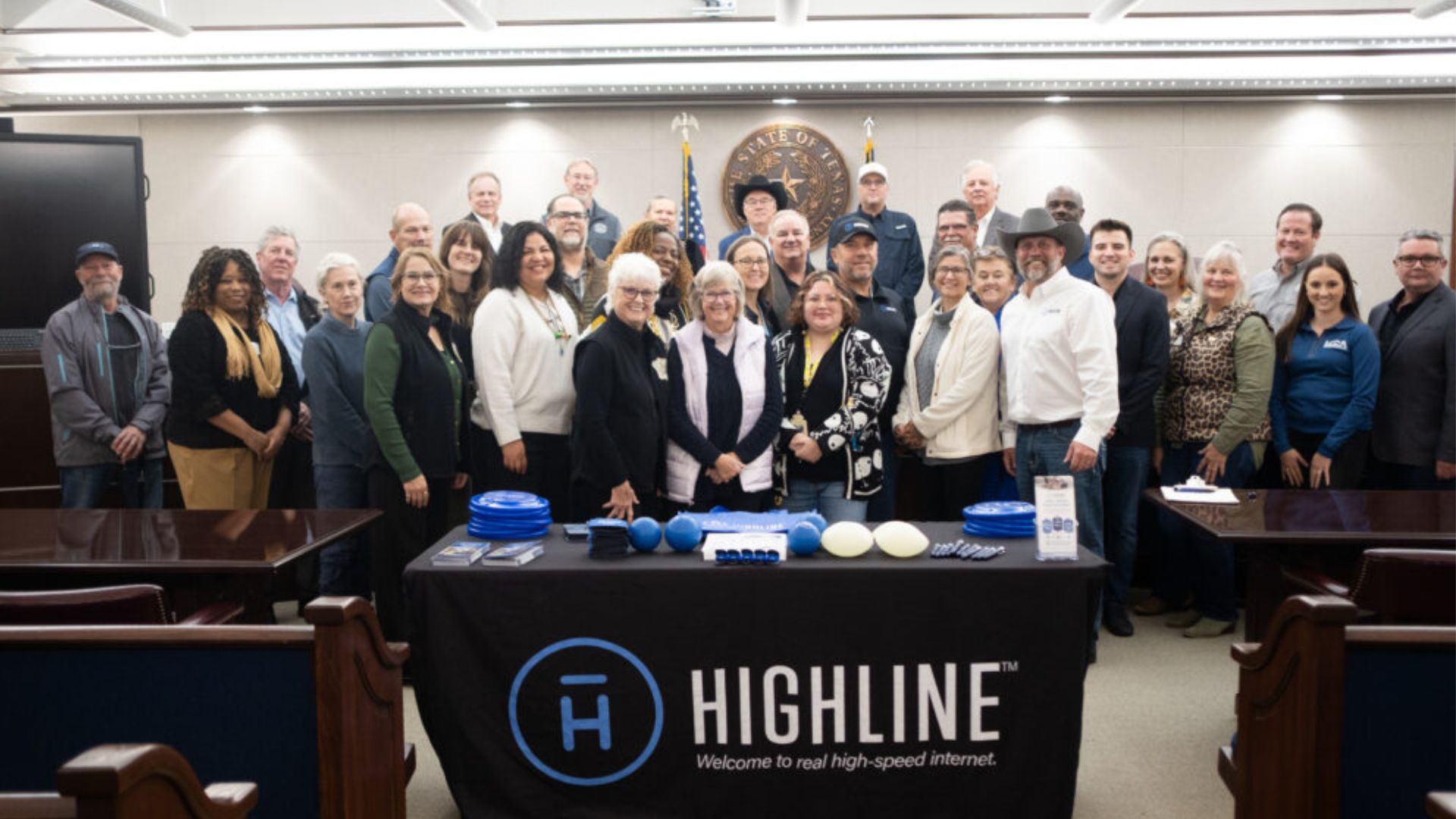 Community partners pose together in a meeting room behind a table displaying Highline internet materials.