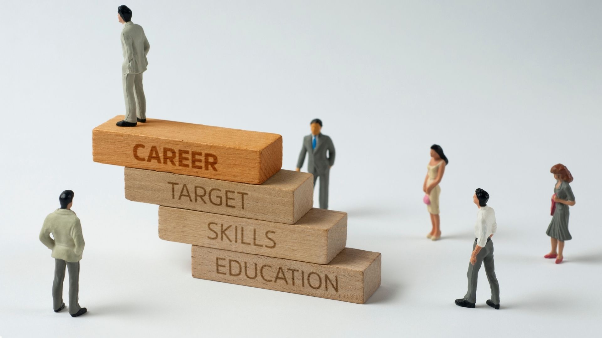 People standing around stacked blocks labeled career, target, skills, and education representing career growth