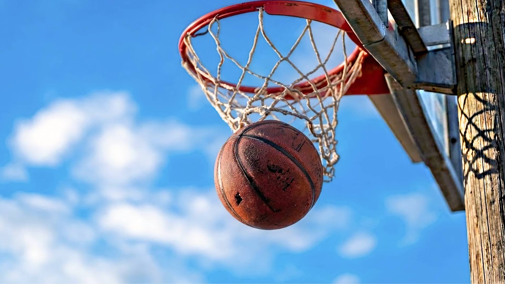 A close-up of a basketball going through the hoop on an outdoor basketball court under a bright blue sky, representing recreation, youth wellness, and community gathering at Stony Point Park.