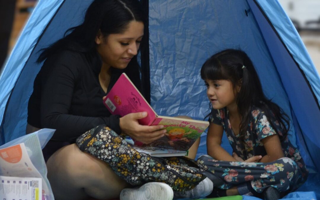 A parent reads a bilingual children's book with their young child inside a reading tent during a Bastrop County Cares family literacy program.