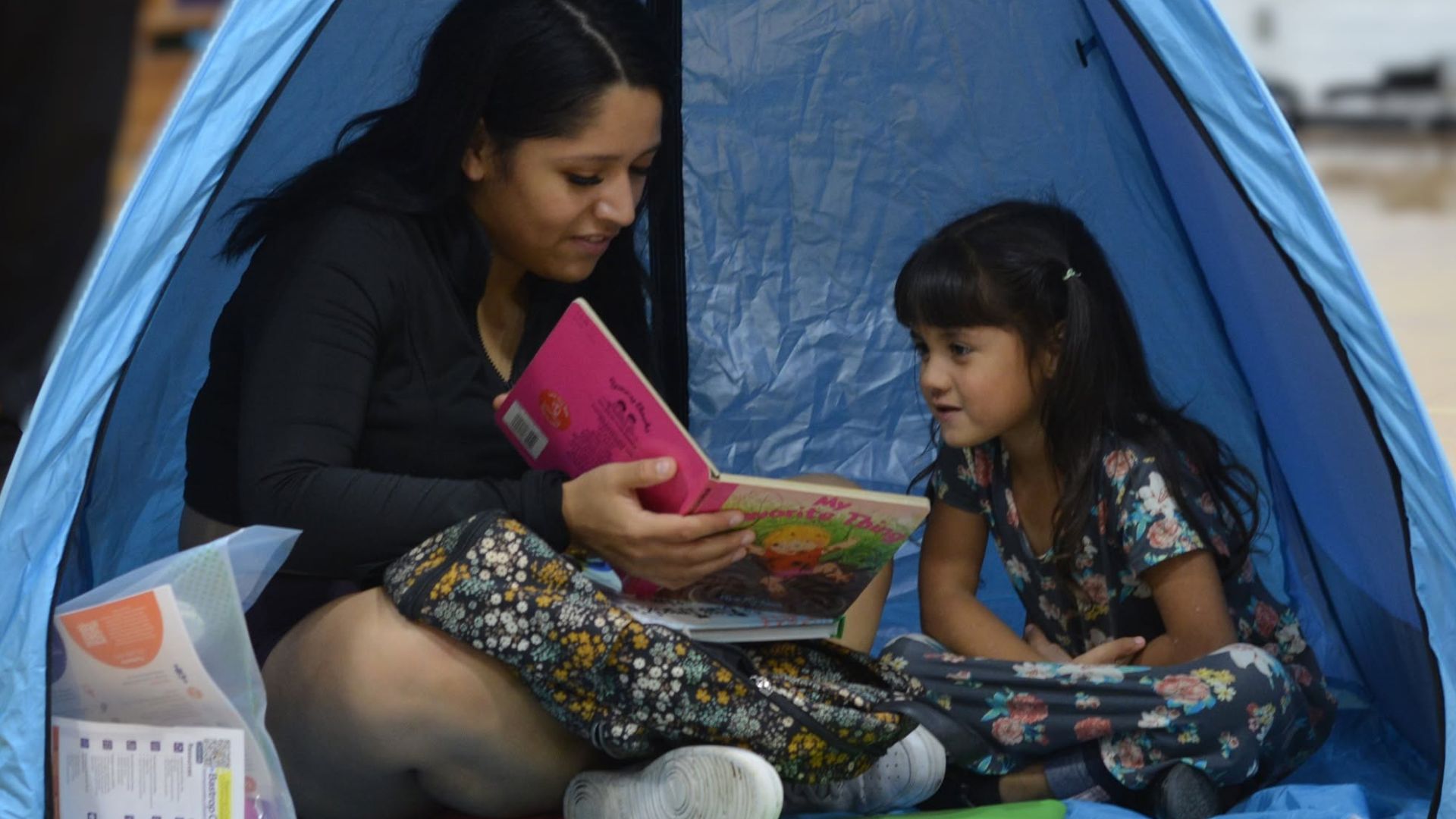 A parent reads a bilingual children's book with their young child inside a reading tent during a Bastrop County Cares family literacy program.