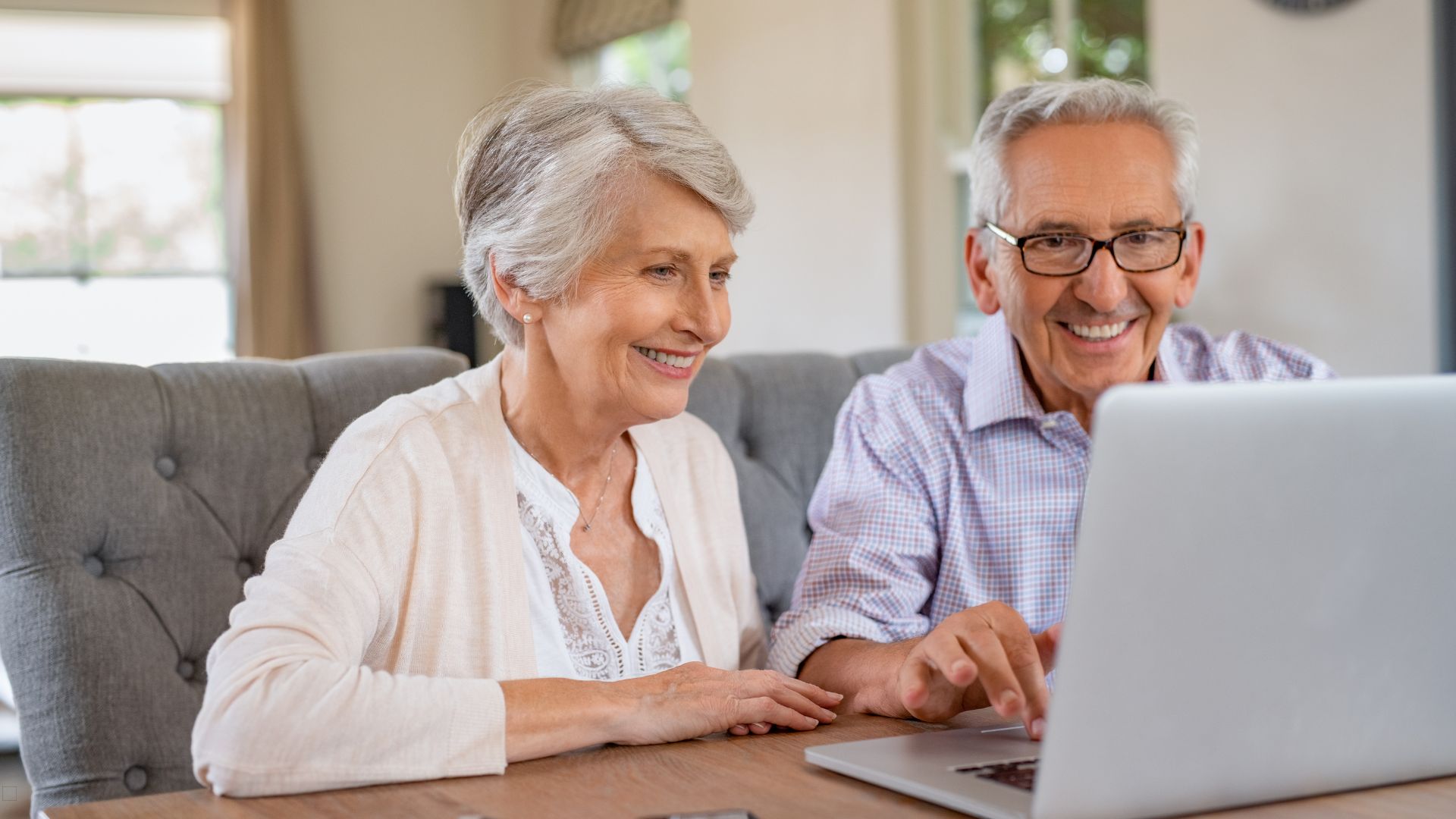 Older adult couple smiling while using a laptop together at home.