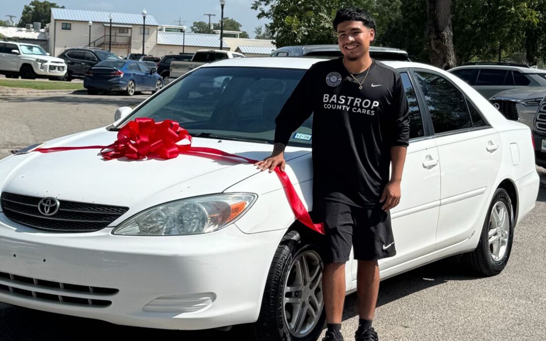 Andrew “Drizzy” Flores, Bastrop County Cares Sports & Recreation leader, standing beside his donated car with a red bow.