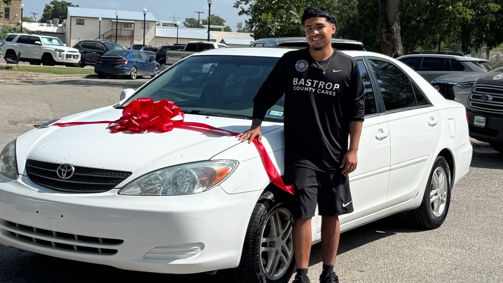 Andrew “Drizzy” Flores, Bastrop County Cares Sports & Recreation leader, standing beside his donated car with a red bow.