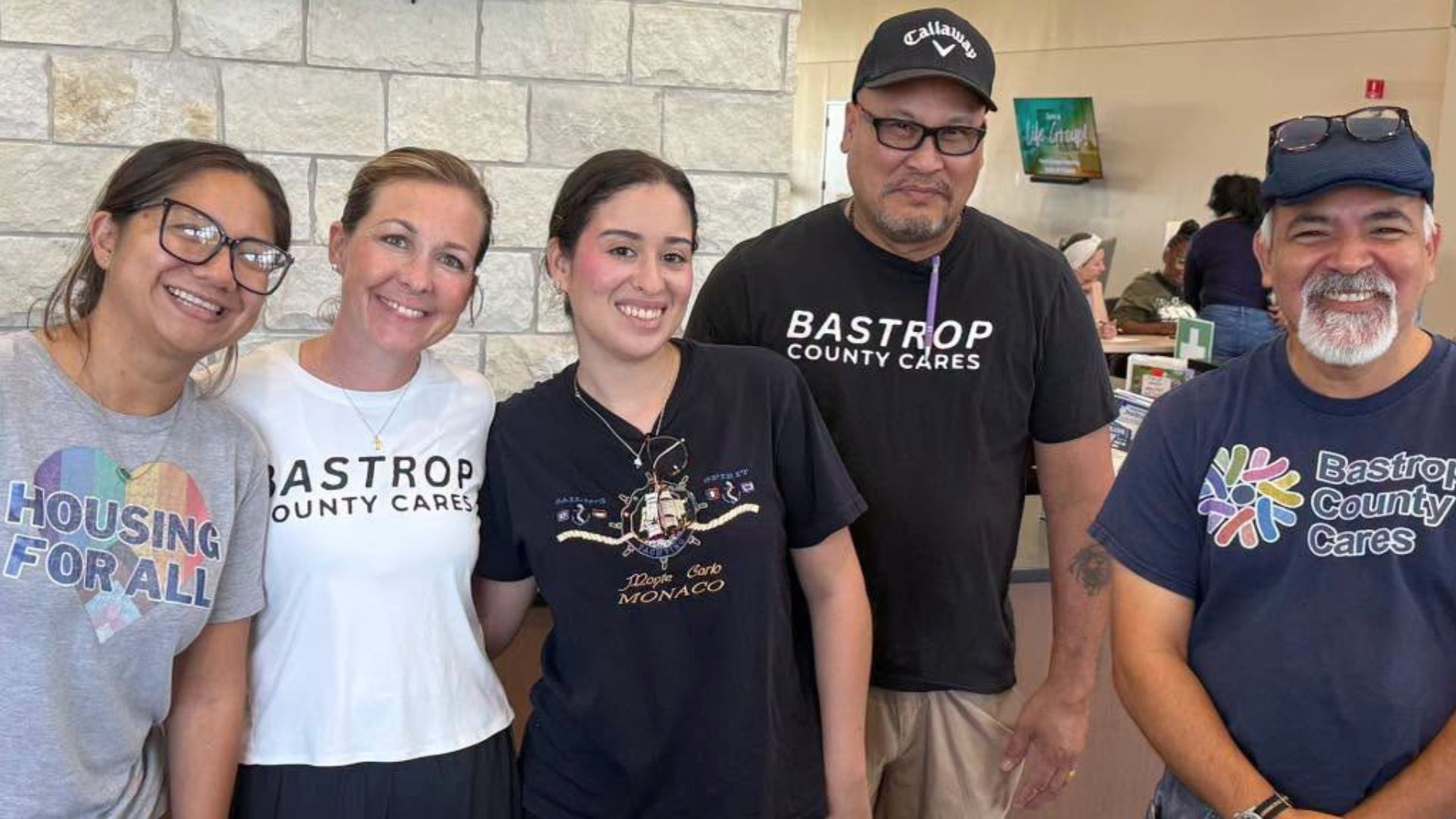 Beige Brown Minimalist Museum Presentation Five Bastrop County Cares team members smiling together at a community event.